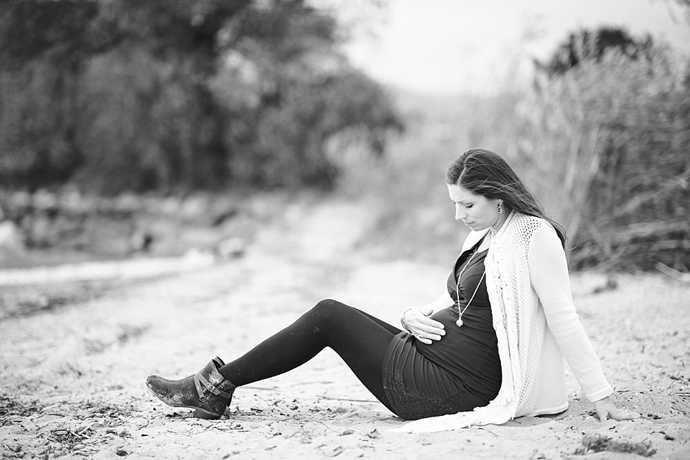 Schwangere junge Frau sitzt im Sand
