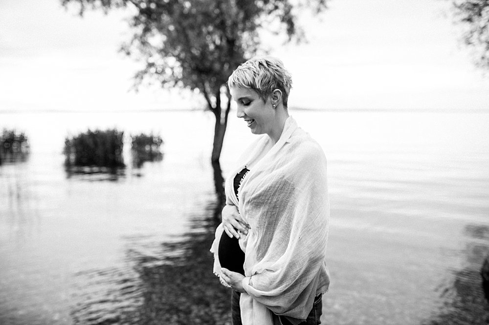Blonde schwangere Frau steht am See und hält ihren Babybauch