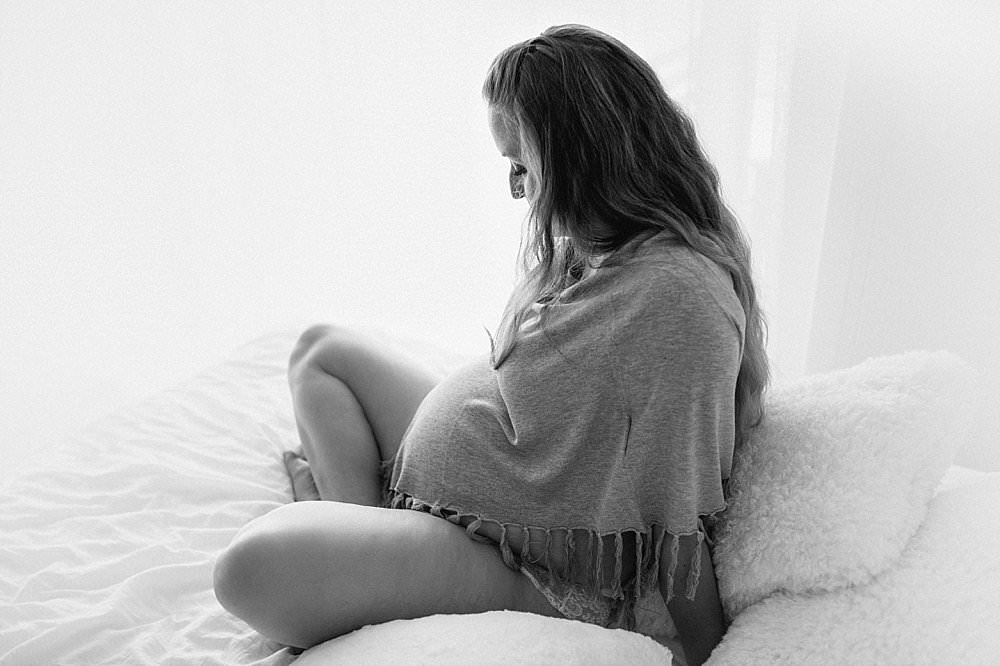 Schwangere Frau sitzt im Schneidersitz auf dem Bett - schwarzweiß