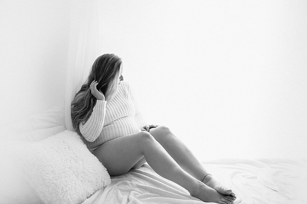 Junge Schwangere sitzt auf weißem Bett - schwarzweiß