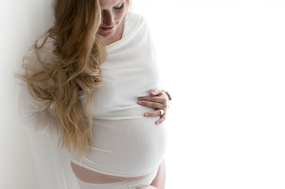 Langhaarige Schwangere betrachtet ihren Babybauch